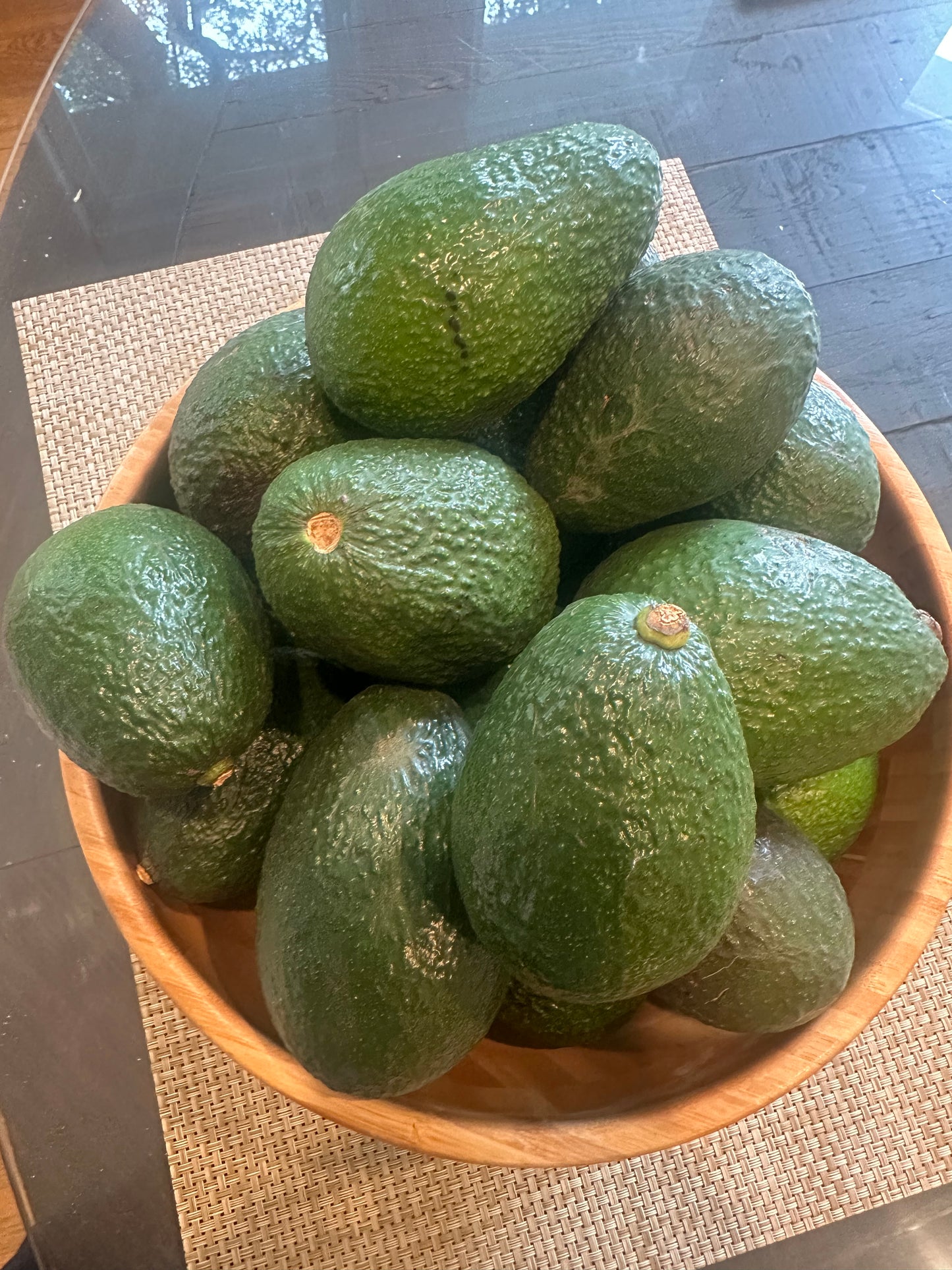 Wooden bowl filled with organic Hass avocados on a dark surface