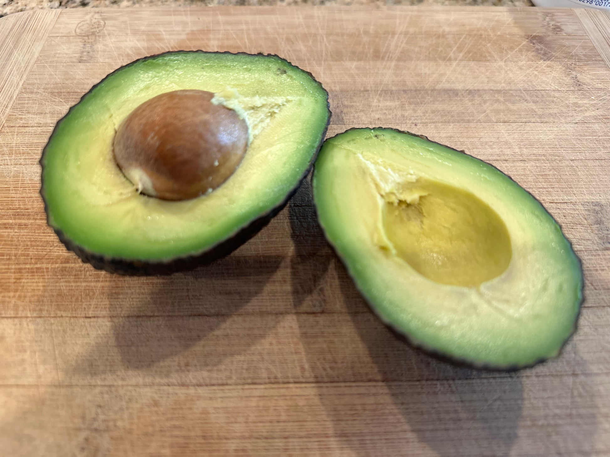 Halved organic Hass California avocado on a wooden cutting board