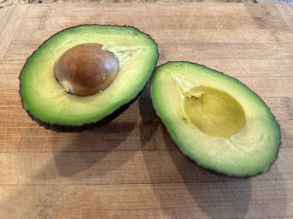Halved organic Hass California avocado on a wooden cutting board